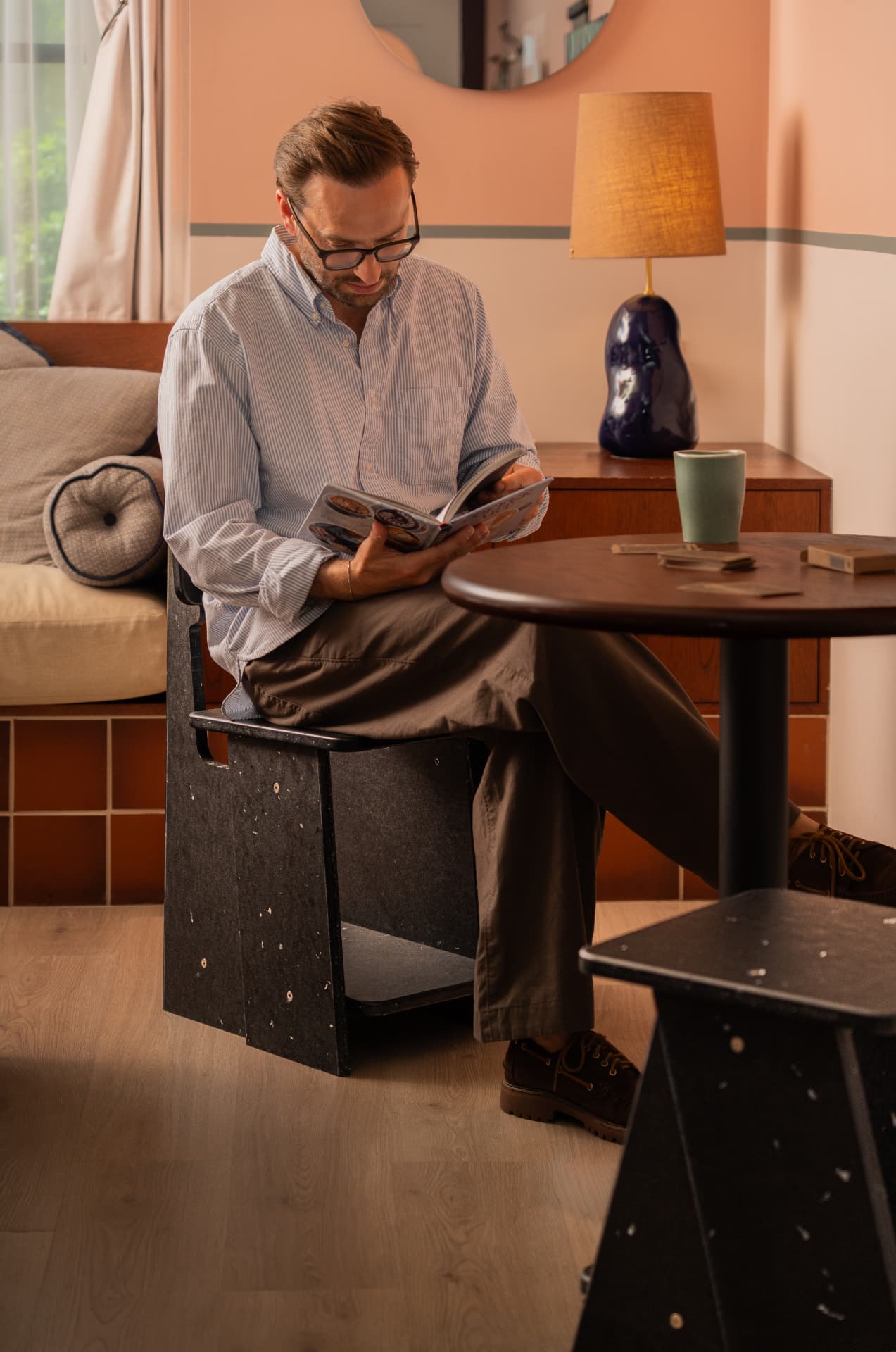A man reads beside a MadeBy recovered-material chair and pedestal table in a warm interior