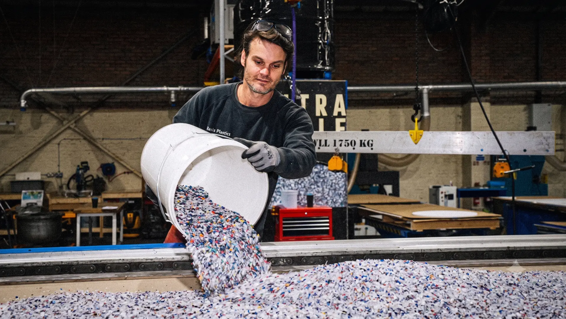 Multi-colour plastic flake poured from a white bucket over a processing bed