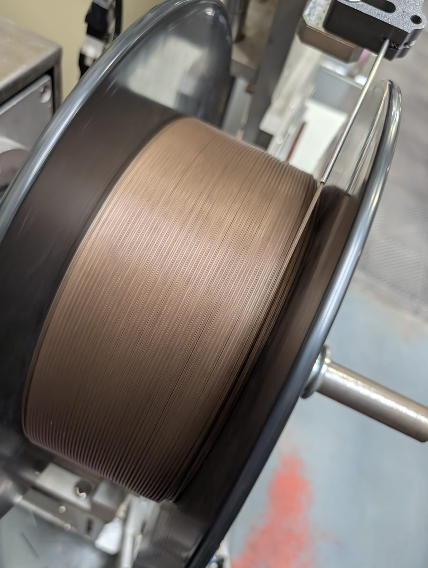 A spool of brown recovered-material filament wound on a metal spindle in a workshop