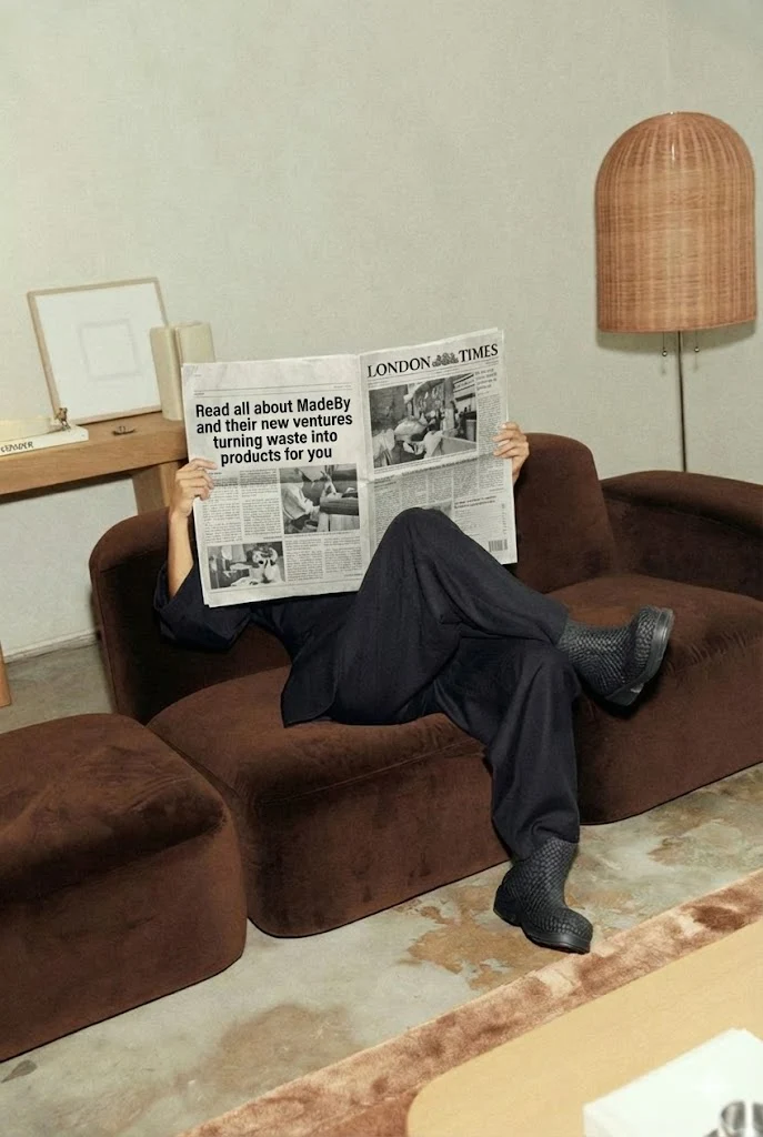 Someone on a brown sofa behind a broadsheet newspaper, with a recycled pendant lampshade beside them