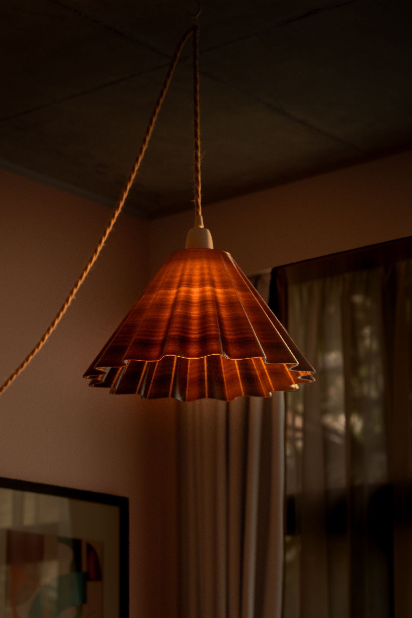 A pleated amber pendant lamp shade glowing in a warm interior, made from compressed coffee waste